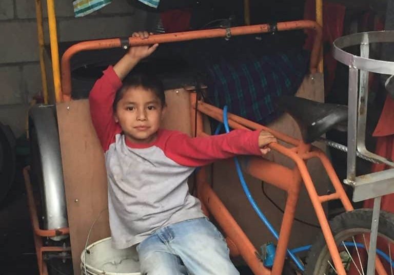 Manuel Manuel leans against the bicycle cart his mother uses to sell hot food. He rides on his mother’s back when she goes into the city.